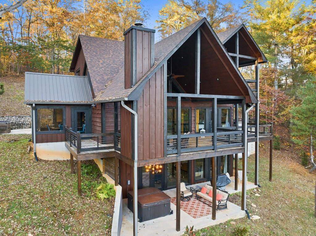 A modern wood cabin with multiple steep roofs and a large wraparound deck surrounded by autumn trees.